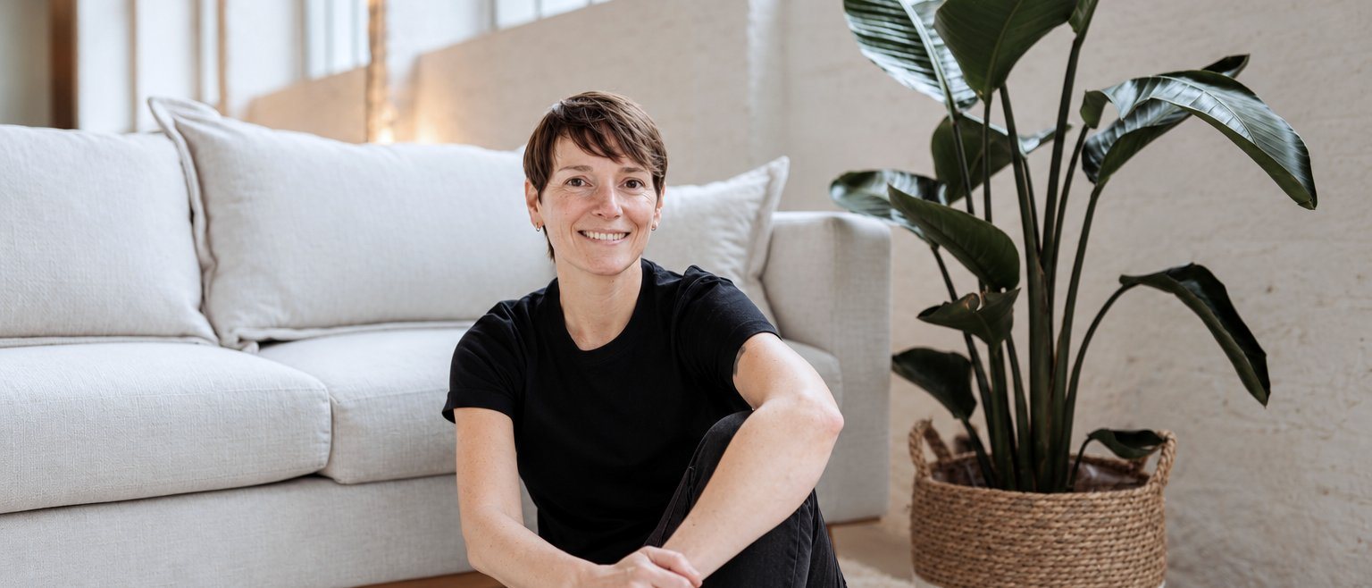 Alexandra Sackmann lächelt in die Kamera, sitzend vor einem hellen Sofa